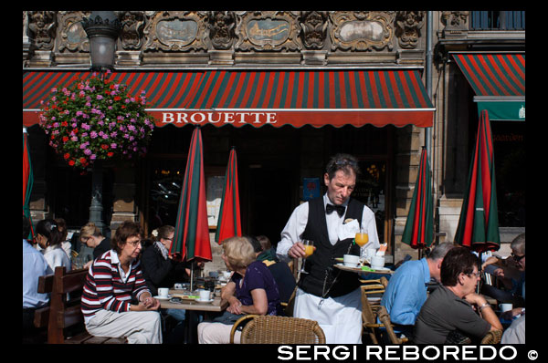 Restaurante en los bajos de los edificios de Louve, Sac y Brouette. Grand Place. El Louve, Sac y Brouette son un conjunto de casas que no fueron reconstruídas en 1695, cuando el resto de los edificios de la Grand Place se renovaron. Debido a la conservación de sus fachadas, se les consideran los edificios más bellos de la Grand Place. CAMARERO SIRVIENDO EL DESAYUNO.