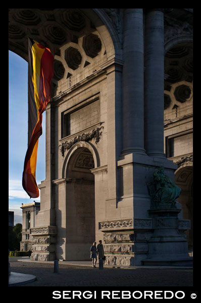 El arco triunfal estaba previsto que estuviera acabado para la conmemoración del 50 aniversario, pero solamente se acabaron las columnas. Para que pareciera acabado se colocaron paneles de madera, y hasta 1905 no pudo ser finalizado. La escultura de la cuadriga que lo corona se llama Brabante levantando la Bandera Nacional, y fue diseñada por Jules Lagae y Vincotte Thomas. PASEANDO POR EL ARCO TRIUNFAL AL ATARDECER.