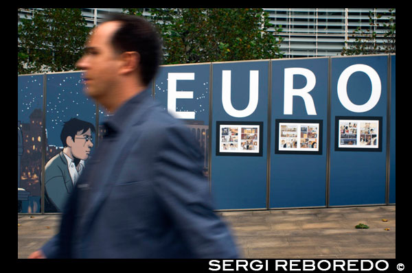 Barri Europeu de Brussel · les. La zona que acull la majoria de les institucions de la Unió Europea és coneguda comunament com el Barri Europeu de Brussel · les o Quartier Européen en francès. El barri del Parlament era una zona tranquil · abans d'esdevenir un lloc clau per a la política comunitària europea. Els grans edificis estan emmarcats per tres grans zones verdes a l'est de la ciutat, el Parc de Brussel · les, el Palau del Cinquantenari i el Parc Leopold. Un dels edificis més representatius de la Unió Europea és l'anomenat Berlaymont. Aquest edifici, amb una planta en forma d'ics i catorze pisos d'alçada, va ser construït el 1967 com a seu de la Comissió Europea. UN HOME PASSEJA AMB UNS POSTERS DE EURO