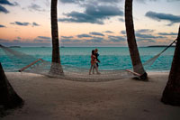 Aitutaki. Cook Island. Polynesia. South Pacific Ocean. Two tourists walk along the beach of the Hotel Aitutaki Lagoon Resort & Spa. A hammock invites you to relax.  The Aitutaki Lagoon Resort & Spa is an all-bungalow resort located in Aitutaki, in the Cook Islands. Akitua is the island on which the resort is located, and is accessible by a ferry that transports people back and forth from the main island of Aitutaki. Catriona Rowntree, the presenter for Australian Nine Network's travel show Getaway has called the resort her favourite destination. A Magical Hideaway. Secluded and romantic, Aitutaki Lagoon Resort & Spa is nestled on its own island in the pristine waters of Aitutaki Lagoon. Our magical hideaway offers luxury accommodation in paradise; over-water bungalows, beachfront suites, lagoon view bungalows and motel style units. With the help of our local people, the bungalows have been decorated with platted kikau for the roofs, hand-woven pandanus wall matting, coconut hemp rope and locally carved artefacts. All bungalows are air-conditioned and have ceiling fans, a mini bar, direct dial international telephone, hairdryer and tea/coffee making facilities. Located in tropical gardens fragrant with frangipani and brightly coloured hibiscus, the lagoon is only steps away through the swaying coconut palms. Or from an overwater bungalow your feet don’t need to touch sand, just dive off your sundeck in to cool, blue water!