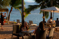 Isla de Rarotonga. Isla Cook. Polinesia . El sur del Océano Pacífico. Los turistas fotografiando el mar y disfrutar de la puesta de sol en la playa del Hotel Crown Beach Resort & Spa. La mezcla de la mejor de la arquitectura antigua y la nueva , las villas con techo de paja de forma inusual en la Playa Corona combinan tradicionalmente inspiradas , con una decoración de primera de cajones . Los bungalows octogonales están impecablemente acabado con paneles de madera clara , muebles de mimbre y obras de arte local en las paredes. Al igual que en otras partes de la isla, se le enfrenta con una elección entre pagar una prima por una posición frente a la playa o la reducción de costes mediante la elección de una villa situada un poco hacia atrás de la arena. Esparcidos por 4,5 hectáreas de jardines privados , las 22 villas se sitúan sensiblemente con mucho espacio entre cada unidad , y los patios privados están angulados todo inteligentemente para una máxima privacidad y unas vistas óptimas isla. El ambiente es elegante y refinado , y es también por lo general considerablemente más silencioso que otros centros turísticos más conocidos de Rarotonga , pero el servicio y las instalaciones son cada pedacito tan bueno como era de esperar para un hotel en este rango de precios. Hay dos restaurantes en el lugar ( la alta cocina Windjammer y un bistró - bar frente a la playa más informal ) , un centro de spa y de masajes, tienda de, un servicio de cuidado de niños, e incluso se puede obtener una introducción al buceo libre los domingos.