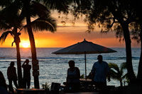 Isla de Rarotonga. Isla Cook. Polinesia. El sur del Océano Pacífico. Puesta de sol en la playa en el Hotel Crown Beach Resort & Spa. Iluminada. Los turistas tomando fotos. Sombrillas. El Crown Beach Resort se compone de 22 villas situado en acres cuatro y medio de jardines tropicales, que da a una hermosa franja de playa de arena blanca. La impresionante piscina tiene unas vistas fantásticas de la playa y el árbol de la llama serena y jardines; un lugar ideal para relajarse con un buen libro. Después de un duro día tomando el sol o bucear usted puede hacer su camino hacia el spa para un masaje terapéutico o tratamiento. Junto con desayuno tropical y té de cortesía por la tarde, este complejo cuenta con dos restaurantes: El Windjammer, que sirve deliciosos pescados del día y pan hecho en casa, y la playa lado Cabana Bar and Grill, para una cena más informal. Cada villa es cómoda autónomo que garantiza el máximo confort, lo que permite disfrutar la calidez y el encanto natural de las Islas Cook en este complejo atento.