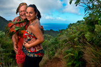 Rarotonga Island. Cook Island. Polynesia. South Pacific Ocean. A tourist with maorí tattoo takes pictures with Mr. Pa.  Ten minutes into my ascent of Rarotonga’s 413m-high ‘Needle’, a dip into the warm waters of the island’s halo-like lagoon is effortlessly topping my ‘must do’ list. But first I need to negotiate the steep and slippery tangle of roots and mini-ravines making up the first half of Rarotonga’s Cross-Island Track. Close behind me is local hiking legend Pa, carrying plenty of fresh papaya and bananas for on-the-go sustenance. Pa is a well-worn nickname, apparently borne out of the frustra- tion his German ex-wife had in pronouncing his much longer traditional name. And like his adopted moniker, everything about Pa is stripped back and simple. No shoes and no fancy hiking gear – just an innate understanding of the mountainous tropical landscape we’re traversing. His unlined face and muscular physique belie the fact that he’s more than 70 years old, testimony to his more than 3700 ascents of the peak, known more formally as Te Rua Manga. After 40 minutes uphill we reach the base of the Needle. Across a series of rugged val- leys, Pa indicates the 653m-high Te Manga, shrouded today in amorphous cloud. 