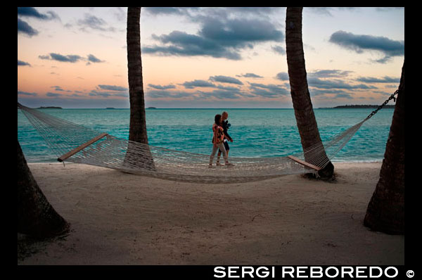 Aitutaki. Cook Island. Polynesia. South Pacific Ocean. Two tourists walk along the beach of the Hotel Aitutaki Lagoon Resort & Spa. A hammock invites you to relax.  The Aitutaki Lagoon Resort & Spa is an all-bungalow resort located in Aitutaki, in the Cook Islands. Akitua is the island on which the resort is located, and is accessible by a ferry that transports people back and forth from the main island of Aitutaki. Catriona Rowntree, the presenter for Australian Nine Network's travel show Getaway has called the resort her favourite destination. A Magical Hideaway. Secluded and romantic, Aitutaki Lagoon Resort & Spa is nestled on its own island in the pristine waters of Aitutaki Lagoon. Our magical hideaway offers luxury accommodation in paradise; over-water bungalows, beachfront suites, lagoon view bungalows and motel style units. With the help of our local people, the bungalows have been decorated with platted kikau for the roofs, hand-woven pandanus wall matting, coconut hemp rope and locally carved artefacts. All bungalows are air-conditioned and have ceiling fans, a mini bar, direct dial international telephone, hairdryer and tea/coffee making facilities. Located in tropical gardens fragrant with frangipani and brightly coloured hibiscus, the lagoon is only steps away through the swaying coconut palms. Or from an overwater bungalow your feet don’t need to touch sand, just dive off your sundeck in to cool, blue water!