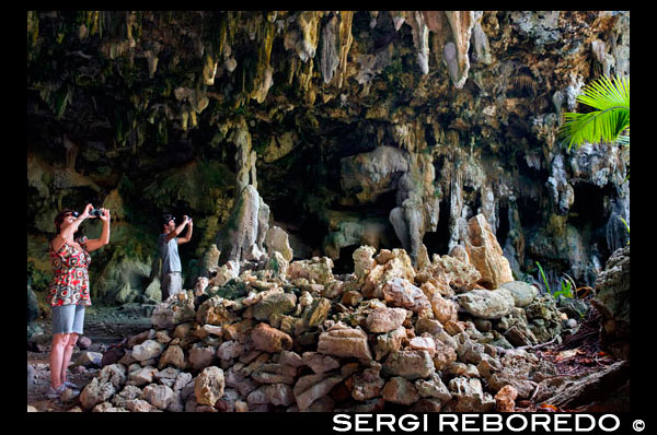 Atiu Island. Cook Island. Polynesia. South Pacific Ocean. Several tourists photographing the impressive Kopeka Bird Caves in Atiu.  These caves are the home to the Kopeka Birds, unique to Atiu. This swift like bird nests deep within the caverns and navigates in the dark by using an echo locating series of clicks. Hear the legend of Inutoto and Tangaroa and learn of the flora and fauna found in the makatea (raised coral) surroundings. Bring your swimwear and enjoy a candle-lit swim in the artesian water pool.  Nurau and Vai Akaruru water caves are fun to swim. Nurau has a vertical sinkhole that drops down from the cave floor to a new level completely underwater. This sinkhole is the entrance to an underwater labyrinth incompletely explored in 1997 by Australians David Goldie and Paul Tobin. Diffuse light filters down to the waters in Vai Akaruru cave making this cave easy to swim. Te Ana O Raka is an easily accessed burial cave. However as Aue Raka's ancestors are interred in this cave it is important to gain permission to enter. Aue offers a tour of the cave and points of interest in the area Ph 33256. Pau Atea cave is long and has many passages. There are many other caves in the area and these are thought to interconnected. It is easy to get lost in these caves. Atiu is a volcanic island surrounded by a coral reef, cliffs and raised coral limestone called makatea. It has taro swamps, lake, limestone caves, lush tropical bush and pristine beaches - some of the finest in the Cook Islands. The narrow, clean lagoon enables you to explore the reef & its sea life, enjoy a beach to yourself and your 'own personal lagoon pool' while you sit back and relax to the sound of the sea as it meets the reef. When sea conditions allow visit the coral gardens and grottos. Swim in the small harbour and, in calm weather, enjoy snorkelling the reef from there or in the coral gardens. In season clearly view, from the beaches & cliffs, the Humpback Whales & Spinner Dolphins when they show themselves. The tropical bush is home to wonderful bird life & exoctic flora. Atiu - 'Enuamanu' which translates the "Island of Birds" has many species including the Kopeka, an echo-locating swiftlet that nests deep inside the caves, the Kakerori, which was introduced to Atiu to help save the Rarotongan bird from extinction and the endangered Rimatara Lorikeet reintroduced from French Polynesia to Atiu in April 2007.