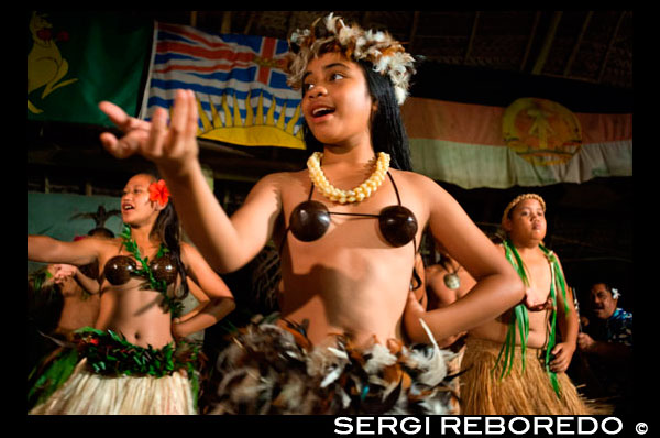 Atiu Island. Cook Island. Polynesia. South Pacific Ocean. Children dressed in traditional Polynesian dances and interpret Polynesian dances organized at Hotel Villas Atiu Atiu island. The Cook Islands lie northeast of New Zealand in the South Pacific Ocean. Cook Islanders are related to the Maori of New Zealand and the inhabitants of French Polynesia (commonly referred to as Tahiti). Cook Islands dance traditions are kept alive through festivals, celebrations and performances for tourists. Cook Islanders living abroad in the United States, Australia and New Zealand perform their dances as a form of cultural preservation.   Dances of the Cook Islands have much in common with other Polynesian dance forms. More widely known dance styles such as the hula from Hawaii and the tamure from Tahiti share similar mythology and dance themes. Cook Island dance performances often include chanting and singing among the dances, which tell stories or serve as spiritual communion with the Polynesian deities. Women’s Choreography: Men and women dance together in performances, though in separate groups. The women’s movements feature side-to-side movements of the hips. These movements are controlled by the knees. The hips must be energetic, with large, pronounced moves, but the upper body must stay graceful, with the shoulders remaining still. Some movement in the arms and hands may accompany the dance, but it must be carefully controlled. Men’s Choreography:  While the women’s silhouette is vertical with movements centered on the hips, men dance closer to the ground, with stronger movements in a distinctive bent-knee pose. The men move their knees in a quick open-and-close fashion. Grass adornments on the lower legs accentuate these moves. Music: Distinctive drum beats propel the traditional dance music in the Cook Islands. Contact with Europeans introduced string instruments to Polynesians, which they adapted into their music. The ukulele became an iconic instrument of Hawaiian music, and is also found in the Cook Islands. However, when recreating traditional dance performances, Cook Islanders choose the drums for authenticity. Fast and slow rhythms accompany the dancers and their bodies must keep time with the music. Drummers in the Cook Islands are highly trained and skilled artists. Though drums provide the background for the dance competitions on the islands. Competitions solely for drummers can be found as well. Costume: Traditional dance costumes of the Cook Islands are of natural fabrics and elements, such as shells, bark, grass, leaves, and feathers. Large belts of leaves around the hips increase the illusion of movement, or a long grass skirt hides the movement of the knees. Traditional costumes leave the men’s chests and the women’s abdomens revealed as a way to celebrate the human form.