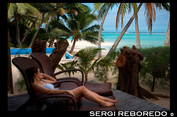 Isla de Rarotonga. Isla Cook. Polinesia . El sur del Océano Pacífico. Un cliente de la mujer se relaja en una tumbona junto al mar en el lujoso Little Polynesian Resort en Rarotonga. En el estilo típico de las Islas Cook, Little Polynesian Resort se encuentra en primera línea de playa de la laguna Titikaveka . Imagínese pasar las horas en el sofá con vistas a las impresionantes aguas color turquesa y playas de arena blanca . Para el alojamiento de Islas Cook lujoso e íntimo que puede `t ir más allá de este romántico resort boutique. Little Polynesian Resort ofrece dos tipos de alojamiento , el jardín se encuentran y el largo de la playa de Son . Todas están bellamente decoradas en tradicional polinesia y diseño isla y mobiliario . El jardín son una unidad escondido en los jardines tropicales y cuenta con una zona de cocina. El largo de la playa de Son se encuentra junto a la playa y cuenta con un gazebo privado con camas de día con vistas a la laguna. Nuestros espectaculares puestas de sol y las noches crepusculares harán de su boda o renovación de aquí , en el corazón del Pacífico Sur, una experiencia muy íntima y única. Si prefiere algo un poco más formal, una boda por la iglesia también se pueden arreglar. Confíe su día especial para nosotros con uno de nuestros paquetes de bodas y nosotros nos encargaremos de todos los detalles , que le da más tiempo para explorar nuestras hermosas islas. Todo lo que tienes que hacer es presentarse en el día. Cada uno de los 10 Luxury Beach Ares viene con su propio gazebo privado y cama de día con vistas a la playa de arena blanca de Titikaveka . Cada Pia Tiare es una unidad de tamaño de estudio amplia, construida como parte de un duplex , que también están diseñadas con inusualmente altos techos, una larga pero casi olvidado de la marca de la arquitectura tradicional de las Islas Cook . De hecho , éstas son las únicas estructuras que queden en el desarrollo turístico original, aunque completamente destruida y reformada a nuestro nuevo estándar de ultra . Aquí, de nuevo cada ventana tiene opciones dobles para ver a través de la configuración de sombra o privadas. Invitando camas king size también se enfrentan a la laguna , mientras que las duchas fuera de las puertas, tinas de hidromasaje bajo las estrellas , bar frigoríficos pre - almacenados y champán a la llegada todos pueden ser parte de la experiencia Polynesian Little . Este complejo ha sido diseñado con todas las oportunidades para aprovechar sus recursos naturales. Los Ares están integradas en el entorno natural de palmeras y follaje tropical. Su terraza se abre a una vista del llamativo color turquesa del océano , las olas fascinantes y todo perfectamente enmarcada con el verde de las palmas por encima y por completo a tu alrededor.