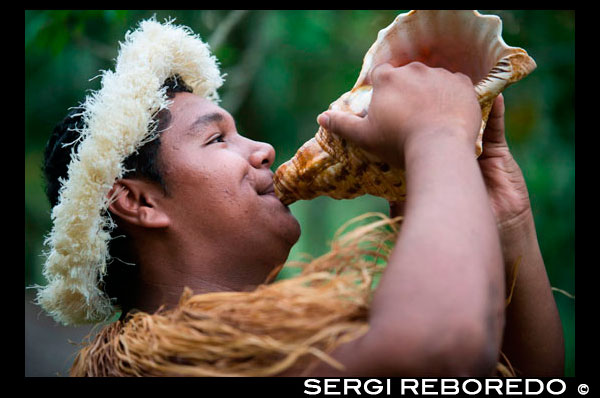 Rarotonga Island. Cook Island. Polynesia. South Pacific Ocean. A Polynesian sounds the conch shell in the Highland Paradise Cultural Village show.  Highland Paradise Cultural Village located on Mangaroa Mountain. This 500 year old village was once lost in time and taken over by the surrounding jungle, but has since been rediscovered and opened to visitors. En route to this 200 acre site, your guide will inform you about the lives of the native Cook Islanders prior to the arrival of the missionaries. Upon arrival at the village, you will begin your immersion into the local culture by learning about the spiritual marae and voyaging skills of the island's forefathers. Here, you will view perfect replicas of village houses as they once stood, along with sacred placs of worship, where battles were fought and the site of human sacrifices. You will also see the High Chief's rock throne and canoe navigator's compass rock along with discovering how important the coconut tree is, the many ways of tying the colorful pareu and how to make flower garlands. You will also have the opportunity to sample some of the local cuisine and tropical fruit. The highlight of your visit will be a passionate and colorful performance of native dancing and music that embraces the true spirit of the island's culture.