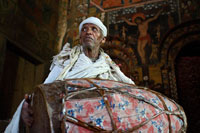 A priest makes drumming inside Debre Birhan Selassie Church (also called the Cherubim. Just outside the town of Gondar is the Debre Birhan Selassie church known for its murals, located on a hill above the city, with beautifully painted walls that have many religious stories. If you look up the eighty heads are winged Ethiopian cherubs smiling, each with a slightly different expression.'s most famous ceiling Ethiopia.