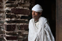 Un sacerdote en la puerta de la iglesia Debre Berhan Selassie. Cuenta la leyenda que, cuando a finales del siglo XIX los derviches sudaneses intentaron destruir esta iglesia, un enjambre de abejas los echó del lugar, persiguiéndoles enfurecidas, hasta que los derviches no tuvieron más remedio que desistir de su intento. Debre Berhan Selassie es una iglesia íntima atiborrada de arte etíope. Vidas de santos, mártires y tradición popular se disputan las paredes mientras que decenas de querubines alados devuelven la mirada al visitante desde el techo. 