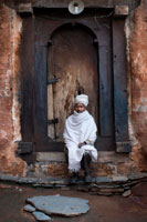 A priest at the door of the church of Abreha Atsbeha, semi carved into the rock. The magnificent church of Abreha wa Atsebha is located 15 km. owest of Wuqro. The church is one of the best and biggest churches in addition to one of the oldest in the Tigray region, dedicated to the famous kings of Axum and brothers and Atsebha Abreha. The church is located in a red rock with a view of the valley and its facade painted white with two blue doors at the height under the arches. The church is decorated with paintings depicting biblical scenes century.