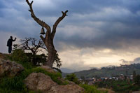 Un hombre fotografía desde un montículo de la ladera de una colina coronada por un viejo árbol del cuelga una gran campana la ciudad de Lalibela. Lalibela y sus iglesias excavadas en la piedra son el corazón de Etiopía, uno de los grandes centros de pelegrinación y el mayor atractivo turístico de la ruta histórica por el país. La ciudad de Lalibela posee el mas extenso complejo de iglesias talladas en la roca de Etiopía, construidas durante el reinado de Gebra Maskal Lalibela y declaradas Patrimonio de la Humanidad por la Unesco en 1978. El rey Lalibela, en el siglo XII, quiso construir una nueva ciudad a la imagen de Jerusalén, en respuesta a la conquista de Tierra Santa por los musulmanes. 