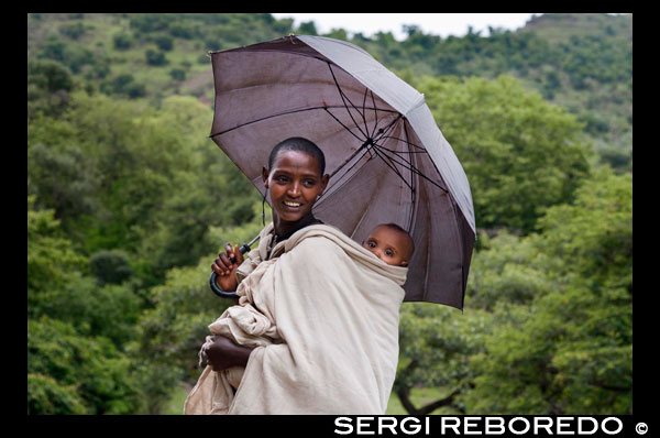 Retrato de una madre junto a su hijo a los pies de las Cataratas del Nilo Azul (río Abay).  Las cataratas del Nilo Azul, en lengua amariña Tis Abay (humo de agua), son uno de esos lugares míticos con los que una sueña cuando lee historias sobre antiguos exploradores, descubridores.. Precisamente, Pedro Páez, un alcarreño nacido en 1564 en un pueblecito de la hoy Comunidad de Madrid, fue el primer europeo "moderno" que estuvo aquí. Era un misionero jesuíta, que se convirtió en un experto de las lenguas y cultura autóctonas, y tuvo la suerte de conocer la sobre fuente del Nilo Azul, en 1613. Tal y como cuentan él y sus compañeros, parece que pocas cosas han cambiado en estos parajes... Bueno, ahora hay una presa para generar electricidad justo encima de las cataratas, y ha hecho menguar su caudal, cómo no... Pero el camino mulero sigue paralelo al río Abbai que discurre entre rocas volcánicas con fuerza... Es el camino por el que echamos a andar, y luego de cruzar el puente que los portugueses levantaron, seguimos caminando y cruzándonos con amhara que van al mercado con sus mercancías (mantequilla, miel...), hasta que, después de subir una pequeña colina, empezamos a oír un ruido de agua, ruido de cataratas, mágico... Poco a poco va subiendo el volumen hasta que ya podemos avistar una de ellas, seguimos avanzando y ahí están, las que por mucho tiempo se creyó que eran las fuentes del Nilo Azul (situadas cerca, en el Lago Tana, aunque no son cataratas...), magníficas, de color marrón porque estamos en la estación de lluvias y arrastran barro y limos, pero bonitas y esplendorosas igualmente.