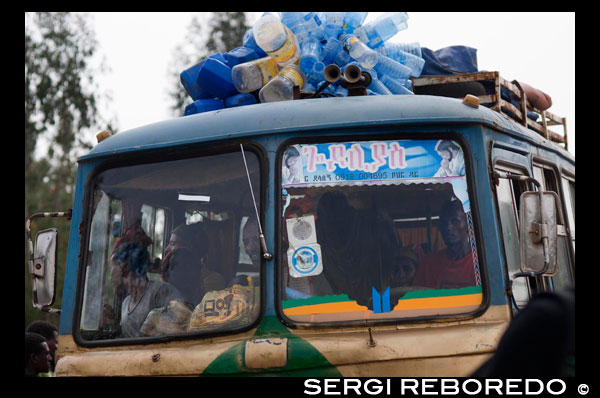 Uno de los típicos autobuses de Etiopia atiborrados de personas y de todo aquello que se puede transportar. Bajo nuestro punto de vista es la mejor forma de vivir el país, pero también debemos decir que es bastante dura, debido principalmente a que los trayectos se hacen inacabables (por ejemplo, en el circuito norte hay recorridos que suponen dos días de viaje). Los autobuses siempre suelen salir alrededor de las 6 ó 7 h. de la mañana y normalmente nunca circulan más allá de las 18 h., ya que se evita la conducción de noche. Para trayectos largos aconsejamos seguir fielmente la ceremonia del autobús: antes de nada es conveniente comprar el billete el día anterior (hasta las 18 h.), aunque los asientos no son numerados e, incluso, se venden más plazas de las que realmente hay. Por esta razón se debe ir a la terminal de autobuses a las 5 de la mañana, entrar en el recinto de la estación antes de que lo hagan los etíopes (la puerta de acceso está cerrada hasta las 5'30 h. pero a los extranjeros se les permite entrar antes de esa hora), dirigirnos al autobús asignado (el billete suele indicar el nº de autobús) y colocarse delante de la puerta a esperar que la abren y permitan el acceso al autobús (a veces podremos entrar inmediatamente, con el autobús todavía vacío, y escoger el asiento que queramos). Sí llegamos a la estación justo en el momento de abrirse las puertas o con posterioridad a este momento tendremos pocas posibilidades de conseguir un asiento, y en cualquier caso no podremos escoger el sitio. Para hacerse una idea de lo que suele pasar en una estación de autobuses etíope cuando se abren las puertas imaginaos la apertura de puertas de El Corte Inglés el primer día de rebajas. No hay compasión de ningún tipo: abuelos, mujeres con niños, y todo el mundo en general, se lanza a una carrera loca para conseguir un sitio. Etiopía es uno de los poquísimos países africanos dónde no se permite ir gente de pie o sentada en el pasillo del autobús, y ésto suele ser respetado porqué hay vigilancia policial en las carreteras para hacer cumplir la ley. Por tanto, todo el que viaja en el autobús debe tener un asiento. En los trayectos largos se suele parar al menos para el desayuno y la comida (un máximo de 20-30 minutos). En trayectos de dos días se para al final del primer día en algún pueblo intermedio a conveniencia del conductor, dónde deberemos buscar algún sitio para dormir. No es demasiado difícil encontrar algún hotel, pero debemos ser conscientes de que son muy básicos. Los autobuses etíopes no son demasiado confortables, especialmente después de unas cuántas horas de viaje. Además, por alguna extraña razón, los etíopes son muy reacios a abrir las ventanas, aunque el calor y/o olor dentro del autobús sean asfixiantes. Esto, unido a la altura y los trayectos sinuosos, hace que algunos pasajeros se mareen a menudo (de aquí que sea habitual verlos oliendo un limón durante buena parte del viaje para intentar evitar el mareo). 