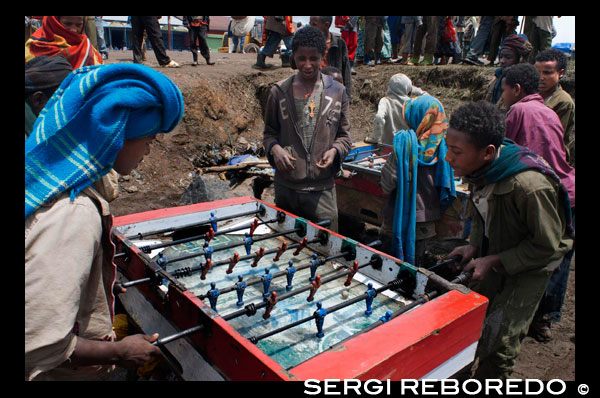 Mercat de Debark. Diversos nens juguen al futbolí mentre els seus pares estan venent o comprant. El poble de Debark és el punt de partida cap a les muntanyes Simien una de les meravelles de Etiopia.Aqui es reuneixen per comprar i vendre els seus productes, el mercat és el cor del poble, el centre d'aquest petit mundo.Aqui es fan camises amb màquines de cosir de les que tenia la teva àvia, es venen espècies, roba, sabates, llana i una infinitat de coses més, és un món d'olor i color.