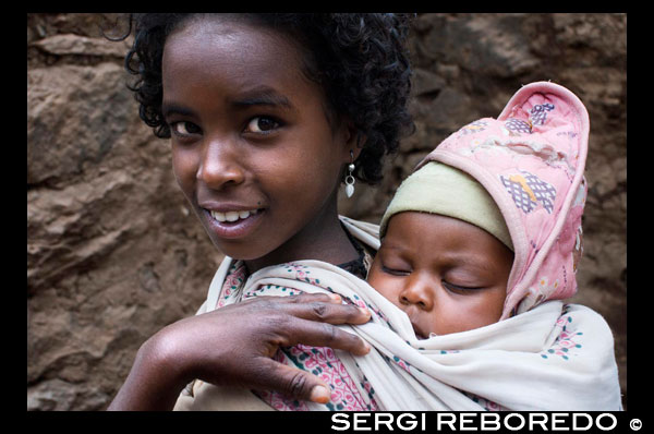 A girl Portea his sister in the village of Yeha, near the ruins of the famous temple. The temple of Yeha, with one side of its walls in ruin, is otherwise still intact and testifies to the advanced level of the people of those times. There is no trace of mortar used to build the temple of the inside of the walls had been believed were paved with gold. Archaeological excavations made ??in 1909, 1947 and 1973 respectively, reveals that this beautiful temple was destroyed by fire. Treasures such as gold rings, golden lions, stone-engraved inscriptions written in Sabean, stone-carved animals like Walya ibex (one of Ethiopia's endemic mammals), pottery works and others were uncovered. Some of these results are displayed in the museum of 4th-century church found in the same compound as the temple while others are displayed in the National Museum in Addis Ababa. The twelve underground formations and four other structures in the deep cave (which seems to lead to Yemen, Lalibela, Jerusalem and Axum), increase the importance of the area for what concerns architecture and history.