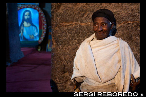 A woman prays inside Bet Medhane Alem church in Lalibela. Bet Medhane Alem or "house of ... Bet Medhane Alem or "House of the Redeemer of the World" is the highest and most extensive of all the churches of Lalibela. Fully carved into the rock, with its 34 meters long by 24 meters wide, is attributed on merit the honor of being the largest monolithic church in the world. Built like a Greek temple is completely surrounded by pillars of square columns. On the stone block is perfectly guess all elements of the temple: The porch, the ships, the vaults and windows and the lavish decoration with reliefs form a unique set. The church is completely surrounded by pillars (the canons of traditional Aksumite period), 18 inside and 18 outside, which for some specialists implies a clear relationship with Hebrew numerology in which 18 would correspond with the numerical value of the word "jai" ("life"). The church has no pictorial decoration interior decoration but based geometric reliefs of the lower windows, combined with alternating square windows and semicircular area is responsible for providing superior beauty inside the temple. In one corner, you can see three empty graves that according to tradition were excavated couple symbolically hold the bodies of the three biblical patriarchs Abraham, Isaac, and Jacob. To some historians, this temple would be a replica of the Cathedral of St. Mary of Zion, Aksum originally located and it was destroyed by the Muslims ...