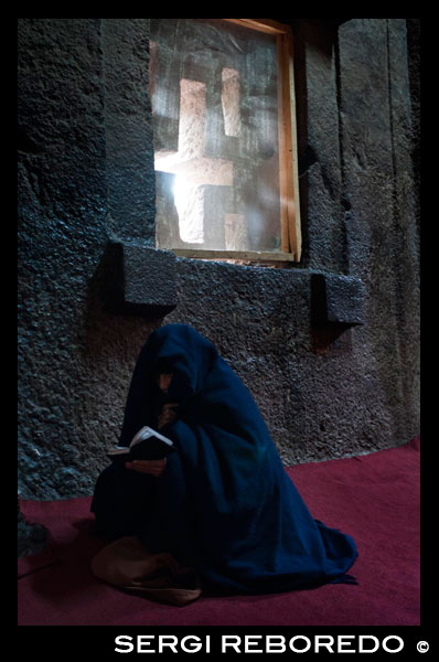 Lalibela. Una mujer reza en el interior de la iglesia Bet Medhane Alem. Para admirar las iglesias de Lalibela no hay que mirar hacia arriba, sino hacia los pies. La iglesia más grande es Bet Medhane Alem, la más grande de todas, con 33 metros de largo por 25 de ancho y una fastuosa decoración que recuerda a los templos griegos. La de Bet Emmanuel, unos centenares de metros al este de la anterior, es una de las más bellas y mejor talladas de todas, que seguramente sirvió como capilla real. Hace más de 700 años, un rey etíope decidió hacer de su ciudad la “Jerusalén” del mundo cristiano ortodoxo. Pero en vez de levantar grandes templos a la manera clásica, se le ocurrió excavarlos en la roca para que los enemigos que hostigaban su reino no los localizaran fácilmente. El resultado fue una de las maravillas de la Antigüedad, un conjunto de once iglesias distribuidas en dos grupos, más una duodécima separada de éstas, que se fueron deconstruyendo a golpe de cincel, vaciando la roca hasta lograr un volumen interior igual al que se hubiera conseguido en un templo clásico, con planta de cruz griega, columnas, capiteles, bóvedas de medio punto y altares, solo que todo es de una sola pieza. El lugar se llama Lalibela, está en una esquina poco accesible del norte de Etiopía, cerca de la frontera con Eritrea, en mitad de unas montañas áridas, pobres y desnudas que apenas verdean durante la temporada de lluvias. Y es uno de los lugares que más me han impactado en mi vida de viajero; uno de esos sitios que recomendaría visitar a cualquiera antes de hacerse viejo. 