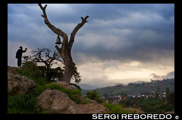 Un home fotografia des d'un monticle de la vessant d'un turó coronat per un vell arbre del penja una gran campana la ciutat de Lalibela. Lalibela i les seves esglésies excavades a la pedra són el cor d'Etiòpia, un dels grans centres de pelegrinación i el major atractiu turístic de la ruta històrica pel país. La ciutat de Lalibela posseeix el més extens complex d'esglésies tallades a la roca d'Etiòpia, construïdes durant el regnat de Gebra Maskal Lalibela i declarades Patrimoni de la Humanitat per la Unesco el 1978. El rei Lalibela, al segle XII, va voler construir una nova ciutat a la imatge de Jerusalem, en resposta a la conquesta de Terra Santa pels musulmans. Molts dels seus edificis històrics van prendre el seu nom d'edificis d'aquella ciutat. La major part d'aquestes esglésies estan íntegrament excavades a la pedra formant un monòlit (una única pedra tot ella) la qual cosa fa d'aquestes esglésies obres úniques, típicament etíops. El conjunt està format per 13 esglésies. La més representativa de les esglésies de Lalibela és la de Beta Girorgios (Sant Jordi) amb planta de creu grega i quinze metres d'altura, tallada íntegrament a la roca i formant una galleda monolític.