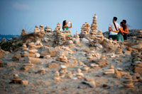 Formentera. Ses Illetes Playa, Islas Baleares, Formentera, España. Retroiluminación de la puesta del sol con piedras de diferentes formas. "El Diluvio" ("La Riada"), un espacio único construido con piedras por parte de la Johannes Schultz alemán. Los turistas toman fotos.