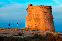 Formentera. Garroveret Tower on suntet. A couple of tourist taken pictures in Torre des Garroveret - one of the towers on Formentera, Balearic Islands, Spain. 