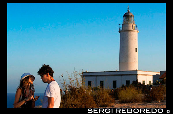 Sunset. Turistas Pareja joven en el Faro, Faro de la Mola, Formentera, Pitiusas, Islas Baleares, España, Europa. Los faros en el puerto de La Savina, La Mola y Es Cap de Barbaria están situados en lugares de incomparable belleza que merecen una visita gracias a su espectacular paisaje. El faro de La Mola es el más antiguo y el más importante. Faro más alto de la isla, que fue construido en una de 120 metros de alto acantilado,. Disfrutar de los amaneceres y puestas de sol desde este punto es una experiencia inolvidable, mágico según famoso escritor Julio Verne, quien usó el faro como escenario de un breve episodio de su novela Héctor Servadac y quién está conmemorado por una placa en el lugar.