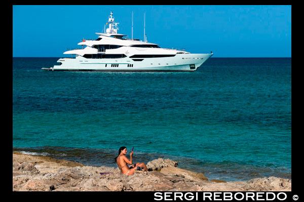 Mujer atractiva que se peina. Playa de Es Pujols, Formentera. Yate de lujo en el agua turquesa en la playa de Es Pujols Formentera mar Mediterráneo Islas Baleares. Frente a la playa se puede divisar pequeños islotes, que ofrece hermosas vistas. Una playa tranquila para toda la familia para disfrutar. También hay una rampa y una silla adaptada para personas con discapacidad para ir en el agua.