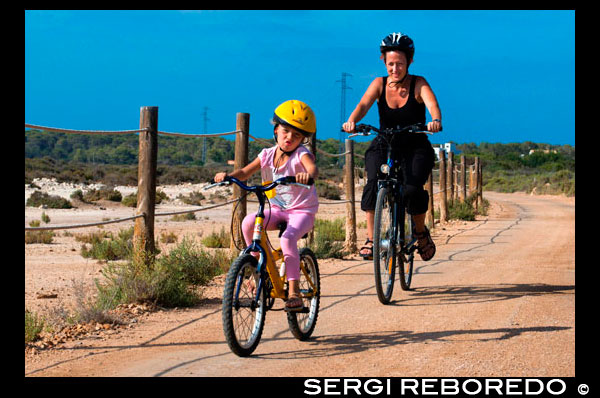 Mother and daughter are riding in a bike. Pudent Lake. Formentera. Balearic Islands, Spain, Europe. Bicycle route. Spain; Formentera; Pudent; lake; road; active; routes; travel; with; child; children; woman; people; cycle; bike; bicycle; island; baleares; balearic; bicycle; kid; kids; people; active; countryside; active; cycle; direct; direction; directions; es; estany; formentera; francesc; free; hike; hiking; holiday; ibiza; indicate; island; islas; la; lagoon; lake; natural; path; paths; point; pointing; pudent; pujols; ramble; route; sant; savina; sign; spain; time; tourism; tourist; vacation; walk; walking; way; Baleares; atrraction; destination; Europe; European; holiday; travel; islands; mediterranean; photos; place; spanish; sun; tourism; touristic; vacation; view; Balearics; beautiful; beauty; paradise; fun; happy; coastal; paradisiac; popular