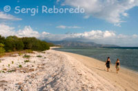 Two women walk along the sandy beach in the west of the island, near the pier Bounty Resort. Gili Meno.