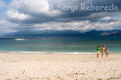 Algunos turistas pasean por la playa de la zona Oeste de la isla, la más desabitada turísticamente hablando. Gili Meno. Gili Meno es una pequeña isla a 2 kilómetros del puerto de Bangsar, en Lombok. Es un viaje fácil en bote, rodeado de plátanos, garrafas de agua y mujeres que llevan provisiones para vender. Una isla de bungalows sobre la playa, donde se puede cenar pescado del día. Una mezquita, una escuela y un café Internet pueblan los caminos interiores, donde viven los isleños. Alguna pareja occidental observa a los pescadores que reparan los barcos sobre la orilla y la gente local saluda a los turistas al cruzarse con ellos. No hay policía en Meno. ¿Para qué?  