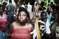 Una mujer con los ojos prácticamente idos se encuentra en trance en las cascadas de Saut d’eau en Ville-Bonheur.  El festival de vudú de Saut d'Eau se celebra cada año el 16 de Julio coincidiendo con el día en el que en 1847 apareció una visión de la Virgen Maria. Miles de devotos llegados de todos los lugares de Haiti se bañan en estas aguas para purificarse o pra perdirle al Gran Maestro que convierta en realidad sus sueños. El vudú es la religión mayoritaria de Haiti. Los adeptos necesitan ser poseidos por un espiritu Iwa para poder comunicarse con el Gran Met, ya que este se encuetra muy alejado del plano físico. En la fotografía una adepta se encuentra poseida por el gran Iwa. Grita y sus movimientos son convulsos. En esta religión, para que un adepto o vodouisant se convierta en sacerdote o houngan necesita primero someterse a una serie de ceremonias de iniciación. Durante el peregrinaje que se lleva a cabo en los días de julio el pueblo se llena de visitantes invadiendo todos los recursos disponibles. Durante el resto del año nadie se acerca a este rincón de Plaine du Cul de Sac, pero en esos días la gente acampa a sus anchas como puede. Algunos vienen provistos de tiendas de campaña, otros duermen en casas de amigos y los más acaudalados y algunos periodistas dormimos en el Hotel Villa Marie Robenson & Georges, un cuchitril de pensión de mala muerte que durante las fiestas hace pagar sus camas al abusivo precio de 100 dólares. Se aprovecha de ser prácticamente el único hotel de la ciudad y muchos deciden visitar el Wozo Plaza Hotel en el cercano pueblo de Mirebalais como mucha mejor reputación y un servicio más ajustado a su precio. 