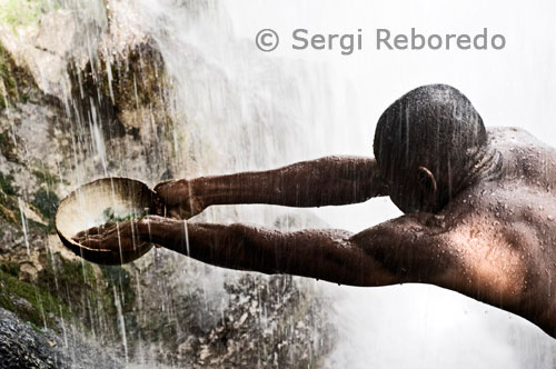 Un hombre recoge el agua que cae de la cascada para purificarse con ella. En esta fiesta de tradición vudú se honra a las diosas Iwa con ceremonias cristianas, como la veneración a la Virgen de los Milagros (conocida aquí como la Virgen del Carmen), en una simbiosis que mezcla el cristianismos con las raices africanas que traidas por los exclavos.En la lengua oficial créole, el término oficial de Vodou se refiere a la religión de Haití. Esta palabra proviene de la voz fon vudu (espiritu divino), que se usa todavía en Benin, cuna africana del vuduismo. Como antiguo reino de Dahomey, Benin proporcionaba los esclavos necesarios que se necesitaban en aquel momento en Haití, los cuales siguieron rindiendo culto a su religión ancestral. Los practicantes, suelen huir del término anglicanizado voodoo (de donde proviene el término español “vudú” por sus connotaciones morbosas y fuera de la realidad.