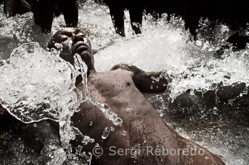 Un hombre poseido por uno de los espiritus del vudú se baña en una de las charcas poco profundas de la cascada de Saut d'Eau. Antes de que pueda invocarse a cualquier Iwa, Legba (el espíritu de los curces de caminos) debe abrir las puertas el mundo espiritual. Después se saluda hacia los cuatro puntos cardinales, agradeciendo la salida y la puesta de sol, y el nacimiento y la muerte.  Entre los Iwas, Agwe es el señor del mar. Además de dar paso a través del agua, presta ayuda a las personas cuando nacen y salen del agua dentro de la madre, y en el momento de la muerte. Los devotos le ofrecen ron, tartas, carneros y su equivalente es San Ulrico. 