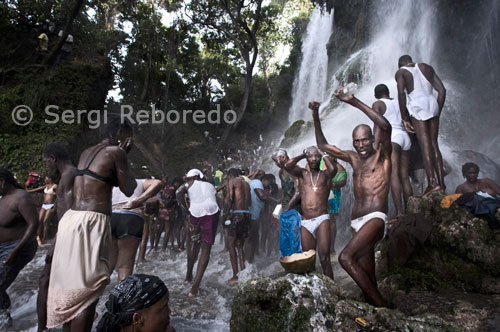 Trepar hacia la cascada de Saut d’eau, de una altura de 30 metros, no es fácil. Como ella, los peregrinos se dirigen a Saut d’Eau para asistir a la primera de las tres grandes celebraciones católicas-vudúes que atraen a gente procedente de todas las partes del país y de todas las clases sociales. Durante el resto del año los haitianos practican ceremonias en templos llamados peristilos, que son una especie de cobertizos que contienen un altar decorado con pinturas Iwa e imágenes de santos católicos junto a piedras, botellas de Ron Barbancourt y atados de hierbas. En medio del peristilo se levanta un poto mitan (poste central), eje entre el mundo celeste y el terrenal y punto por donde los Iwa penetran en el recinto. Los peristilos están consagrados a una rama determinada de Iwa y decorados en consonancia con pinturas en puertas y paredes y banderas colagadas.