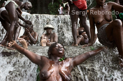 Una de las asistentes al festival vudú de Saut d’eau entra en trance. El festival de vudú de Saut d'Eau se celebra cada año el 16 de Julio coincidiendo con el día en el que en 1847 apareció una visión de la Virgen Maria. Miles de devotos llegados de todos los lugares de Haiti se bañan en estas aguas para purificarse o pra perdirle al Gran Maestro que convierta en realidad sus sueños. El vudú es la religión mayoritaria de Haiti. Los adeptos necesitan ser poseidos por un espiritu Iwa para poder comunicarse con el Gran Met, ya que este se encuetra muy alejado del plano físico. En la fotografía una de las asistentes reza sin ropa. La ropa vieja se suele tirar al agua para luego, despues de purificado, vestirse con ropa nueva. El Vodun o Vudú es una forma teísta y mágica del animismo que se desarrolló entre las tribus de África occidental antes de la época histórica, en los territorios de lo que fuera el Reino de Dahomey (actual Benin). El área cultural de los pueblos Fon, Gun, Mina y Ewe comparten concepciones metafísicas comunes, centradas en torno a la idea de un principio cosmológico dual de orden divino. Por un lado encontramos al Dios Creador (cuyo nombre puede variar, pero que definiremos como Mawu) y por otro lado a una serie de Dioses o espíritus Actores, hijos del Creador. El Dios Creador constituiría así el principio cosmogónico, aislado de los asuntos mundanos, y los Voduns son los dioses o espíritus actores que rigen sobre las cuestiones terrenales.