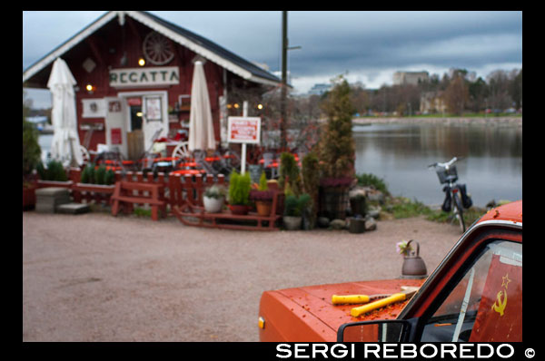 Helsinki. Exterior del pequeño Café Regata, uno de los cafes más visitado de la ciudad.  ¿Qué podría ser mejor en este hermoso domingo que estar sentado en un café en la playa, bebiendo de su taza de café y pasteles tener finlandés delicioso mientras disfruta del sol? El mejor sin duda, el lugar más acogedor y único para que sea Regatta Café entre el monumento de Sibelius y el estadio de remo de edad. La tradicional casa de madera roja al lado del agua es fácil de encontrar. El interior de madera simple da un ambiente acogedor de inmediato. En el mostrador te casera pulla finlandés (pasteles) y las bebidas. Los precios son razonables. Usted tiene que pagar en efectivo, aunque ya no tienen un lector de tarjetas allí. Si el sol brilla definitivamente debe sentarse en la terraza de ensueño. Usted puede tomar un asiento en una de las pequeñas mesas o sentarse junto al fuego vínculo que la luz todos los días. Aquí incluso te invitan a la parrilla sus propias salchichas y carne! Regatta es realmente merece una visita! 