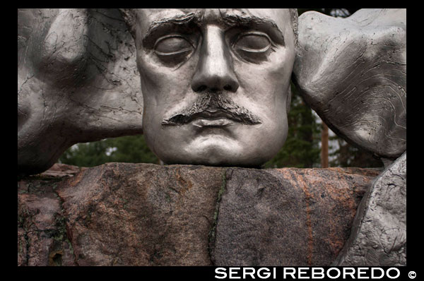 El monumento a Sibelius se encuentra en el parque del mismo nombre (Sibelius Parken), cercano a la costa oeste de la ciudad. Una de las vías desde las que se puede llegar es precisamente desde la calle dedicada al compositor (Sibeliuksen Katu). El barrio, llamado Taka-Töölö, es una zona tranquila fundamentalmente residencial, poco poblada en vida de nuestro autor. El hospital donde trabajaba su hermano Christian estaba en esta zona, y era habitual encontrar a Jean Sibelius paseando. De ahí la elección. En el mismo barrio podemos encontrar además calles dedicadas a los poetas Topelius y Leino. El parque recibió el nombre del músico en 1945, en conmemoración de su ochenta aniversario. Años después de su muerte se pensó en incorporar una estatua importante al parque, para lo cual se realizó un concuerso (años 61 y 62). Hubo un debate sin precedentes en Finlandia sobre cómo debía ser la escultura, si figurativa o abstracta. La ganadora entre 50 proyectos, la artista Eila Hiltumen (1922-2003) decidió incorporar ambas estéticas realizando un monumento en dos partes, una con el rostro del compositor (en su aspecto de los años 10), mientras que la otra consistiría en un símbolo abstracto formado por una serie de tubos, ambas elementos del conjunto metálicos (acero inoxidable). El monumento se inauguró en 1967 y fue tan polémico como las ideas sobre su creación. Lo más llamativo fue la poca importancia y aislamiento que tenía el rostro del compositor sobre los tubos, más grandes y llamativos, y a unos pasos. "Además, ¿qué significan esos tubos?", se preguntaron los finlandeses. Hiltumen no quiso desvelar su sentido, y murió hace unos pocos años sin desvelarlo. Los fineses han sostenido y sostienen aún varias teorías al particular: 1) Son tubos de órgano, el rey de los instrumentos y símbolo por excelencia de la música (instrumento al cual Sibelius dedicó apenas cuatro obras, sin embargo). 2) Representa la aurora boreal, el símbolo de la magia del norte (referenciada en la cantata "Oma maa" ["Nuestra patria"] opus 92) . 3) Son cristales de hielo (referenciados en varias obras del autor). 4) Son un símbolo de los bosques nórdicos (referenciados en Tapiola y en multitud de otras obras). Caben incluso otras propuestas, y ustedes seguro que están pensando en alguna. Puede que esta fuera realmente lo que pensó la artista, el no crear nada concreto y así permitir a los visitantes del monumentos pensar lo que quisieran sobre su significado e inspiración. Con el tiempo la polémica claudicó, y el monumento fue aceptado como un claro homenaje al maestro, y una señal de identidad de la ciudad, del país y de la cultura finesa. Todos los días decenas de autobuses de turistas de los lugares más distantes llegan al parque, y el conjunto artístico, sobre el verde césped o la nieve - dependiendo de la época del año, lógicamente -, sobre una roca salvaje, es mostrado con orgullo al ciudadano del mundo. Una réplica del mismo, a menos tamaño se puede encontrar en la sede de la Unesco en París, lo que denota la importancia cultural y representante de la cultura finesa que tiene la obra escultórica. Quizá el sibeliano, el que acude a Finlandia en busca de lugares impregnados de la presencia del maestro, este monumento puede decir poco, a pesar de su gran simbolismo. Sin duda encontrarán más oportuno visitar el Museo Sibelius de Turku / Åbo (museo de la música de Finlandia, con una sala dedicada a nuestro compositor con manuscritos, cartas, fotografías, y más material de primera magnitud), la casa natal en Hämeenlinna, y sobre todo Ainola, residencia de nuestro músico los últimos 50 años de su vida, donde compuso gran parte de su obra y donde está enterrado junto a su mujer Aino. La casa se conserva prácticamente igual de como la dejó el compositor tras su muerte, con infinidad de recuerdos materiales. En otro momento hablaremos de Ainola con más detalle. 