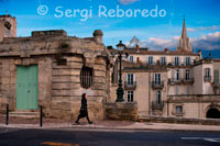 Casas bajas ubicadas junto al Boulevard du L. Vialleton con vistas de la iglesia de Saint Anne.  Aquí la vidilla que tiene Montpellier se disfruta de día, con sus jardines, sus plazas abarrotadas de gente, las terrazas en las calles, etc. Pero, de repente, se hacen las 19.00h y todo el mundo se prepara para cerrar sus negocios y la ciudad se va apagando poco a poco (porque la iluminación de la ciudad deja bastante que desear ciertamente, que a veces da hasta miedo ir por las calles). Ahora, eso sí, en plena navidad (que aquí empieza como en \"El Corte Inglés, o sea, en noviembre jaja) las calles y árboles se llenan de miles de lucecillas, bolas gigantes de navidad colgando de las ramas y los adornos navideños custodian los escaparates de las tiendas. Con respecto a la arquitectura de la ciudad es bastante diferente a la española, donde predominan más las casas bajas o de unos 4 pisos como mucho; las calles son bastante anchas e interminables, de estas que no ves nunca el final, y en las que el \"gran arquitecto\" que las diseñó se empeñó en plantar árboles gigantescos en medio de la acera y poner las farolas entre ellos, con lo cual os podéis imaginar la visibilidad del peatón por las noches.