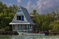 Casa sobre pilons sobre l'aigua amb panells solars i una densa vegetació tropical al fons, Bocas del Toro, el mar Carib, Panamà. Cabina tropical sobre el mar Carib, a l'arxipèlag de Boques del Toro, Panamà. Aquest és el moment ideal per visitar aquestes illes, a viatjar en el temps i perdre en un dels centenars de llocs meravellosos que es poden gaudir. És un lloc únic per trobar a tu mateix; la seva exuberant vegetació tropical, la fauna només es troba en aquesta part del món, les oportunitats per al busseig i el snorkeling l'oceà immillorable Carib