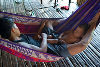 El hombre y su hijo haciendo una siesta en una hamaca en el pueblo de la Native Indian Tribe Embera, Embera Village, Panamá. La gente de Panamá Embera Indian Village Indígena Indio Indios nativos americanos nativos lugareños locales Chagres Nacionales Parque. Embera Drua. Embera Drua se encuentra en la cuenca alta del río Chagres. Una presa construida sobre el río en 1924 produjo el Lago Alajuela, el suministro principal de agua para el Canal de Panamá. El pueblo está a cuatro kilómetros río arriba desde el lago, y rodeada por un parque nacional de 129.000 hectáreas de bosque tropical primario.