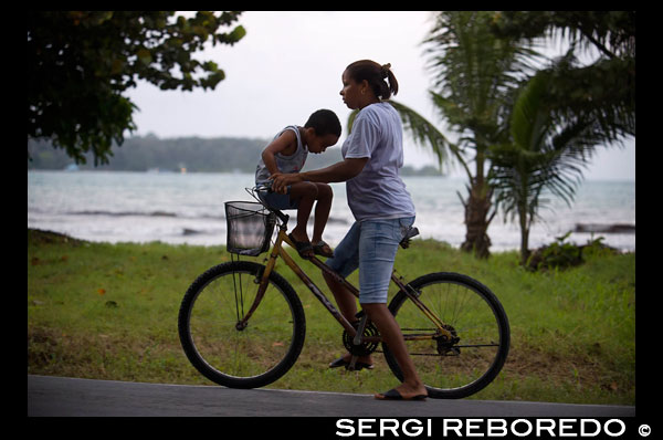 Madre con su hijo en una bicicleta. Bocas del Toro, Panamá. Bocas del Toro (que significa "Boca del Toro") es una provincia de Panamá. Su extensión es de 4,643.9 kilómetros cuadrados, que comprenden el continente y nueve islas principales. La provincia consiste en el Archipiélago de Bocas del Toro, Bahía Almirante (Bahía de Almirante), la Laguna de Chiriquí (Laguna de Chiriquí), y la tierra firme adyacente. La capital es la ciudad de Bocas del Toro (o Pueblo de Bocas) en Isla Colón (Isla Colón). Otras grandes ciudades o pueblos incluyen Almirante y Changuinola. La provincia tiene una población de 125.461 a partir de 2010 Cristóbal Colón y su tripulación primero visitó la zona en 1502 Bocas del Toro limita con el Mar Caribe al norte, la provincia de Limón de Costa Rica, al oeste, la provincia de Chiriquí, al sur, y Ngöbe-Buglé al este. El Río Sixaola forma parte de la frontera con Costa Rica. Un viejo puente del ferrocarril atraviesa el río Sixaola y Guabito entre, Costa Rica. El puente es un paso fronterizo utilizado por los turistas que van entre los destinos en Bocas del Toro y Costa Rica. La provincia contiene dos parques nacionales, Isla Bastimentos National Marine Park y el Parque Internacional La Amistad. El Instituto de Investigaciones Tropicales Smithsonian opera una estación de investigación en Isla Colón justo al noroeste de Pueblo de Bocas. Hay muchas plantaciones de banano en Bocas del Toro, a menudo llamado el oro verde, o el oro verde de América Central.