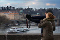 Praga romántica. Un pareja de fotografía en el Puente de Carlos.  El Puente de Carlos (en checo Karl?v most) es el puente más viejo de Praga, y atraviesa el río Moldava de la Ciudad Vieja a la Ciudad Pequeña. Es el segundo puente más antiguo existente en la República Checa. La necesidad de un nuevo puente surgió luego de que el viejo Puente de Judith fuera destruido por una inundación en 1342. Este puente de estilo románico había sido bautizado en honor a la esposa del rey Ladislao I. Astrólogos y numerólogos determinaron que Carlos IV debía asistir al asentamiento de la piedra fundamental a las 5:31 AM del 9 de julio de 1357. Este preciso momento puede ser enunciado como 135797531, y conforma una secuencia capicúa de dígitos impares ascendentes y descendentes, que se encuentra grabada en la torre de la Ciudad Vieja. La construcción fue supervisada por Peter Parler, y liderada por un "magister pontis", Jan Ottl. 