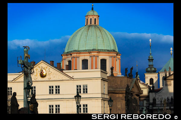 Vistas de la Iglesia de San Nicolás desde el Puente de Carlos.  La Iglesia de San Nicolás de Malá Strana (no debe confundirse con la de Staré M?sto) está considerada la construcción barroca más bonita de Praga. Si la Catedral de San Vito es la obra maestra del gótico, la Iglesia de San Nicolás lo es del barroco. La construcción de la iglesia comenzó en 1673 por orden de los jesuitas, siendo los primeros edificios terminados el edificio parroquial y la escuela. Aunque las obras finalizaron en 1752, se comenzaron a oficiar misas en 1711. En la plaza de acceso a la iglesia se encuentra la Columna de la Peste con la estatua de la Santísima Trinidad. Fue construida en 1715 por Alliprandi. El interior de la Iglesia de San Nicolás está repleto de arte, desde las pinturas en sus techos y bóvedas hasta las esculturas que adornan las paredes. El arquitecto creador del conjunto fue K. I. Dientzenhofer, siendo esta iglesia su obra maestra. 