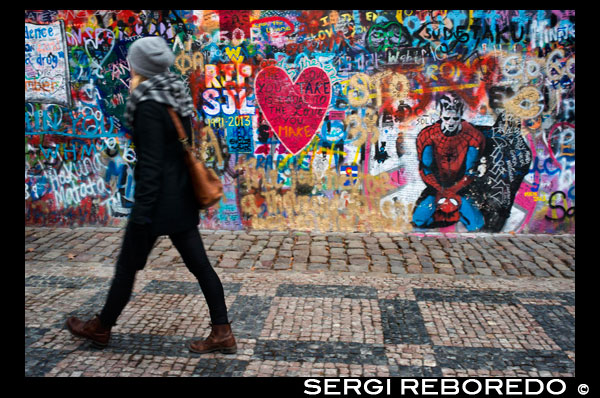 Una chica pasa junto al Muro de John Lennon en el centro de Praga. El Muro de John Lennon es una pared, que en su día fue una más de las que se podían encontrar en cualquiera de los edificios del barrio de Malá Strana en la capital de la República Checa: Praga, pero que desde principio de los años 80 recibe este nombre al ser continuamente decorada con nuevos graffities inspirados en la figura de John Lennon y con pedazos de canciones de los Beatles. El muro se encuentra situado en la plaza Velkop?evorské nám?stí, frente al Palacio Buquoy que alberga la embajada francesa y es propiedad de los caballeros de Orden la Cruz de Malta que permiten que se sigan pintando ininterrumpidamente nuevos graffities en el mismo. El origen del muro tal y como se le conoce hoy se remonta a la fecha en la que John Lennon es asesinado en 1980. El líder de los Beatles era venerado como un héroe por los pacifistas de centro y este de Europa en una época en el que las autoridades comunistas de estos países prohibían incluso la reproducción de las canciones del mismo por su mensaje considerado como subversivo. Tras la muerte de Lennon, en el muro apareció un retrato del artista junto a pintadas con frases desafiantes hacia las autoridades. La policía comunista procedió al borrado de las mismas pero cada vez que lo intentaban, las pintadas volvían a repetirse apareciendo además pedazos de canciones de los Beatles así como dibujos de flores, mensajes pacifistas y otras expresiones de la juventud de la época. Ni tan siquiera la instalación de cámaras de vigilancia nocturna pudo evitar que las pintadas se repitieran cada vez que eran "limpiadas" por las autoridades. Hoy el muro se entiende no sólo como un memorial a la figura de Lennon, sino como también un monumento a la libertad de expresión y a la rebelión no violenta que la juventud checa interpuso ante un régimen autoritario. En 1998 el mal estado de la pared original hizo que tuviera que ser rehabilitada, pero tras dicha rehabilitación las pintadas volvieron a aparecer inmediatamente. Markéta Lehecková.  