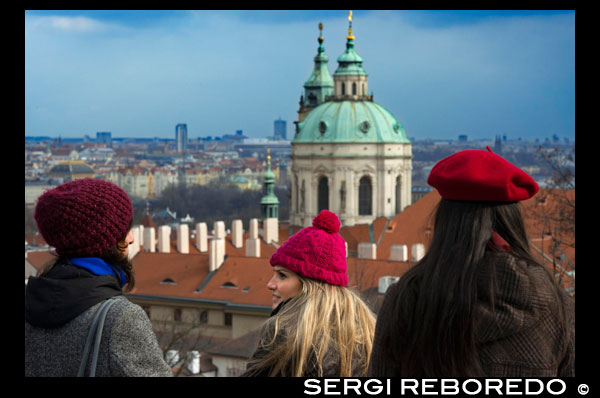 Vistas de la Iglesia de San Nicolás y del Barrio de Mala Strana desde el Castillo de Praga.  Perderse por Mala Strana, al caer la tarde un mes de invierno, es disfrutar de una experiencia única en Praga. La tenue luz de sus calles, el alumbrado público del barrio ayuda, y mucho, al ambiente, es retroceder al pasado, imaginarse cabalgando por sus calles y oir el estruendo de los cascos de un caballo sobre los adoquines. La luz, la arquitectura, la ausencia de tráfico en las calles más interiores, nos brindan una experiencia casi de película, el pasear por sus calles silenciosas, tenues, el pasar por la puerta de un mesón checo y oir el bullicio en su interior y como la luz que sale de sus ventanas iluminan tu pasear. Mala Strana conserva ese aire romántico difícil de olvidar, silencioso, lleno de pequeños cafés, donde tomarse un rico chocolate caliente en un ambiente literario único. 