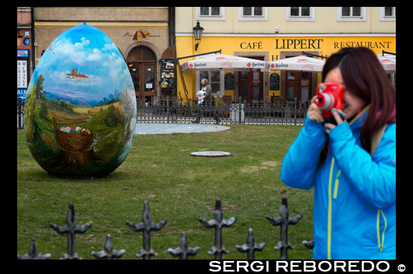 Una japoneses treu fotografies amb una Polaroid als jardins situats davant del Cafè Lippert davant de l'Old Town Square. La Plaça de la Ciutat Vella (en txec: Staromestske námestí (· i)) és una plaça històrica situada a la Ciutat Vella de Praga a la República Txeca. Està situada entre la Plaça de Wenceslao i el Pont de Carles, la plaça de la Ciutat Vella de Praga està usualment plena de turistes durant l'estiu. Oferint diversos estils arquitectònics com el gòtic a l'Església de La nostra Senyora al davant del Týn i el barroc a l'Església de Sant Nicolau, la plaça és un oasi per als viatgers cansats de les estrets carrers de Praga. Entre diverses esglésies, els turistes poden trobar en aquesta plaça el Rellotge Astronòmic, mentre que la torre de l'Ajuntament vell ofereix una vista panoràmica de la Ciutat Vella. Al centre de la plaça es troba una estàtua del reformador religiós Jan Hus, que va ser cremat viu per les seves creences. L'estàtua es coneix com a Monument a Juan Hus va ser erigida el 6 de juliol de 1915 al 500 aniversari de la seva mort. La plaça no és només un popular punt de trobada, també es realitzen en ella algunes celebracions (Any Nou), mercat de festivitats (Nadal i Pasqua), i protestes. En algunes ocasions es mostren jocs d'hoquei i futbol en pantalles gegants, atraient una multitud de fanàtics.