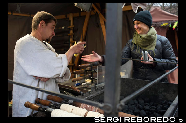 A woman buys delicious trdelník at a street stall. One of the sweets are trdelník Prague. Some cupcakes rolled and hollow, plated sugar, flour, nuts and cinnamon. In this position made ??them great. Trdelník (also known as Skalicky trdelník) is a cake tradicioal of Slovak cuisine (on the border of Slovakia and Moravia) .1 This is a rolled dough on a wooden skewer (whose name is Trdlo) and handle (Rotisserie) a charcoal fire while rotating mass on itself. The final form is that of a fire massecuite cylindrical and hollow inside, slightly smoky flavor with cinnamon and aromatzado. It is very traditional in street markets (in Prague), and is usually served as street food. Markéta Lehecková.