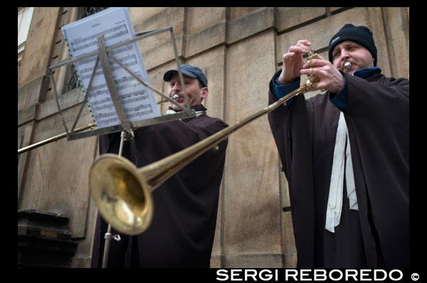 Dos músicos vestidos de clericós y entonado melodías con largas trompetas promocionan un concierto de órgano en la Iglesia de San Francisco de Asís.  También conocida como iglesia de San Francisco de los Cruzados de la Estrella Roja, esta iglesia barroca, dedicada al primer mártir católico incorporado a la liturgia de Bohemia, fue construida a mediados del s.XVII por el arquitecto y pintor francés J.B. Mathey. Situada en la Plaza de los Cruzados (Krizovnicke namesti), formó parte del monasterio de la orden de los Caballeros Cruzados de la Estrella Roja, quienes se encargaban de vigilar el antiguo Puente de Judith (en el emplazamiento del actual Puente de Carlos). En el interior de esta iglesia destaca, además de su cúpula con el fresco de El Juicio Final, un órgano barroco único de 1702, que es el segundo órgano más antiguo de Praga. Diferentes personalidades, como W.A. Mozart, A. Dvo?ák y J.F.N. Seger entre otros, tocaron este órgano, actualmente restaurado. 