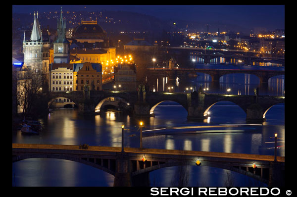 Vistas nocturnas de los diferentes puentes de la ciudad de Praga cruzando el Rio Moldava.  El puente más conocido que se alza por encima de la corriente del río Vltava es el puente de Carlos. Sin embargo no es el único. En la ciudad de Praga hay, de hecho, diecisiete puentes que cruzan el río Vltava. En nuestro recorrido los conoceremos todos siguiendo la corriente desde abajo arriba. El puente que se halla más abajo se encuentra en Zbraslav, en el extremo sur de la capital, a pocos kilómetros del centro de Praga. Antes, al no formar parte de la capital, Zbraslav era el lugar predilecto de excursiones para los praguenses. El puente de Zbraslav es el primero que se sitúa en el territorio de la capital checa desde el sur. Lleva nombre de "Puente de la Carrera de la Paz" según la prueba ciclista que recorre el territorio de la República Checa. Otro puente, que une la orilla izquierda del Vltava con el barrio praguense de Braník, suele ser llamado "Puente de la Inteligencia", por trabajar en su construcción en los años 50 del siglo XX personas cultas como médicos, filósofos y juristas perseguidos por el régimen comunista.  Puente de Barrandov El puente de Braník es el puente ferroviario de hormigón más grande de toda Europa. Sin embargo, el puente no se utilizaba tanto, los trenes iban incluso por un solo carril de los dos que tenía. Es por ello que el puente en la actualidad no está en buen estado. Otro puente que atraviesa el Vltava se conoce como "Puente de Barrandov" y enlaza el barrio residencial de Barrandov con la orilla derecha. Construido en los años 80 del siglo XX, es el puente más grande de Praga y, respecto a la corriente del río, también el más oblicuo. Además se suele considerar como el más feo. El puente de Barrandov es una importante encrucijada que une dos autopistas principales de la República Checa. No obstante, es también un punto de grandes atascos de tráfico, dado el número creciente de vehículos que circulan en la capital checa. Subiendo el río hacia el centro de Praga, encontramos el segundo puente ferroviario, denominado "Puente ferroviario de Vysehrad". Fue construido en la segunda mitad del siglo XIX para conectar las dos principales estaciones de tren a ambas orillas del Vltava. Une asimismo el barrio de Smíchov con el barrio de Vysehrad, presidido por el recinto del mismo nombre.  Puente de Jirásek El quinto puente de nuestro recorrido lleva el nombre de Frantisek Palacký, una de las personalidades más destacadas del renacimiento nacional checo del siglo XIX. El puente es de piedra y el tercero más viejo de Praga. Es el primer puente que ya alcanza en la orilla derecha un barrio histórico praguense - la Ciudad Nueva. El puente, que conduce del barrio de Smíchov en la orilla izquierda, desemboca en la orilla derecha en una plaza con el monumento a Frantisek Palacký. En la Segunda Guerra Mundial el puente se deterioró por los bombardeos. Los grupos escultóricos que decoraban en aquel entonces los extremos del puente, fueron rehabilitados y colocados en el recinto de Vysehrad. También el siguiente puente deriva su nombre de una personalidad de letras. Se llama "Puente de Jirásek", según el escritor checo de los siglos XIX y XX que se hizo famoso por sus tradiciones y leyendas del pueblo checo. El monumento al escritor se halla frente al río, a la orilla derecha, cerca de la casa donde escribió sus obras. Es el último puente que une el barrio de Smíchov con la orilla derecha, de nuevo con la Ciudad Nueva. Es también el comienzo de la principal arteria que recorre el interior de Praga y en las horas punta suele estar repleto de coches.  Puente de las Legiones Otro puente por el centro de Praga se llama "Puente de las Legiones", en alusión a los legionarios checos de la Primera Guerra Mundial. Antes hubo en su lugar un puente de cadenas que llevaba el nombre del emperador Francisco I. El puente sirve de enlace entre dos barrios históricos - el de la Ciudad Pequeña en la orilla izquierda y el de la Ciudad Nueva. Cerca del extremo derecho del puente se halla el imponente edificio del Teatro Nacional. El Puente de las Legiones está decorado con diez postes de alumbrado antiguos, hechos de hierro fundido, de diez metros de altura. Pasa por la Isla de los Tiradores, donde se encuentra el palacio de Zofín, donde se organizan grandes bailes. El puente más viejo y famoso y, según la consideración general el más bello de Praga, es el Puente de Carlos. Sin embargo, en su lugar hubo dos predecesores. El primer puente de la capital checa existía ya en el siglo X y estaba construido de madera.  Puente de Carlos El primer puente de piedra checo y el segundo precursor del de Carlos se llamaba "Puente de Judit", según la reina checa que lo mandó edificar en el siglo XII. El puente fue destruido por una inundación en 1342 y sus restos se pueden ver hasta el presente en el subterráneo del monasterio contiguo. Carlos IV no tardó en hacer iniciar la construcción del nuevo puente, hoy conocido como puente de Carlos. Sin embargo, al principio era llamado "Puente de piedra", ganando su nombre actual tan sólo en el siglo XIX. El inicio de las obras del puente corrieron a cargo del arquitecto imperial Petr Parlér y la construcción fue completada a principios del siglo XV. El puente fue decorado con varias estatuas en el mismo siglo, no obstante la mayor parte de las estatuas fueron colocadas sobre los pilares del puente en la época barroca, en el siglo XVIII. Hay 31 estatuas en el puente de Carlos, incluyendo santos, patronos checos y monarcas. Las estatuas son mayoritariamente de piedra arenisca, excepto dos, una de mármol blanco y otra de bronce.  Vltava Otro puente de nuestro recorrido une la Ciudad Pequeña con la Ciudad Vieja desembocando cerca de la Casa de los Artistas o Rudolfinum, centro del festival musical "Primavera de Praga". El puente lleva el nombre de Josef Mánes, pintor checo que, entre otros, decoró el Reloj Astronómico de Praga. El primer puente de Praga, construido en estilo art nouveau lleva el nombre de Svatopluk Cech, escritor checo del siglo XIX. Conecta el barrio portuario de Holesovice con la Ciudad Vieja y es el punto de partida de los guías turísticos que empiezan allí sus recorridos por el casco histórico en el margen derecho del río. El puente es el más corto de Praga y el nivel de las dos orillas es desigual. Muy parecido es el puente que conduce del barrio de Holesovice a la línea divisoria entre la Ciudad Vieja y la Ciudad Nueva. El puente era primero de cadenas y llevaba el nombre del emperador Francisco José I, tras la Primera Guerra Mundial fue remodelado y comenzó a llamarse "Puente de Stefánik".  Viaducto de Negrelli Milan Rastislav Stefánik era astrónomo, político y aviador eslovaco y una de las figuras importantes de la República Checoslovaca entre las dos guerras mundiales. Dos primacías ostenta el "Puente de Hlávka", denominado según el arquitecto y fundador de la Academia de Ciencias, Josef Hlávka. Es el puente más ancho de la República Checa y el primer puente que atraviesa el Vltava construido de hormigón. Une el barrio de Holesovice con la Ciudad Nueva, pasando por la isla Stvanice, famosa por situarse allí el primer estadio de invierno checo. El siguiente puente es un viaducto ferroviario. Se llama "Viaducto de Negrelli" en honor a su arquitecto, Alois Negrelli, que proyectó también el Canal de Suez. Es el segundo puente más viejo de Praga y el primer puente ferroviario que cruza del Vltava. También fue el puente más largo de Europa hasta 1910. Se extiende entre el barrio de Karlín y el de Bubny. Otro puente de nuestro recorrido es el "Puente de Liben" y enlaza el barrio del mismo nombre en la orilla derecha con el barrio de Holesovice en el margen izquierdo. Es el puente carretero más largo de Praga y fue construido en estilo cubista.  Puentes de Praga (www.czechtourism.cz) Los mismos barrios de Praga, Liben y Holesovice, están conectados por otro puente ferroviario, llamado "Puente ferroviario de Holesovice". Muy cerca se halla el "Puente de los luchadores de las barricadas", el penúltimo de nuestro recorrido. Une el barrio de Holesovice con el barrio residencial de Trója. Deriva su nombre de la barricada que los praguenses defendieron a finales de la Segunda Guerra Mundial. Su lucha heróica la recuerda un monumento situado a la orilla derecha del río. El último puente que cruza el Vltava en el territorio de Praga es el "Puente de tranvías de Holesovice", destinado sólo para este medio de transporte. Para completar nuestro recorrido, debemos mencionar la pasarela peatonal de Trója que cruza el río Vltava desde la Isla Imperial y desemboca en el barrio de Trója, cerca del Parque Zoológico y el Jardín Botánico de Praga. El número de puentes de Praga no es fijo, ya que para resolver la situación insatisfactoria del tráfico en la capital checa, está prevista la construcción de otros dos puentes en la parte norte y sur de la ciudad. 