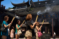 God Temple and pagoda, buddhist temple in Shanghai, burning joss sticks, incense. A women prays and laughs at Chenghuang Miao or City God Temple in Yu Yuan Gardens bazaar Shanghai, China. Located next to the Yuyuan Garden and also known today as the Yu Garden Market, the City God Temple (Chenghuang Temple) was built in the fifteenth century during the Ming Dynasty. Originally a temple built to honor the Han statesman Huo Guang (68 B.C.) The City God Temple is a Taoist temple which is composed of many halls such as the Grand Hall, Middle Hall, Bedroom Palace, Star Gods Hall, Yama Palace, Xuzhen God Hall. The temple had an area of more than 10,000 square meters including two gardens: West Garden (Yuyuan Garden) and East Garden. The City God Temple has a great influence on the residents of Shanghai. The religious festivals of the temple are considered to be the festivals for all Shanghai people.